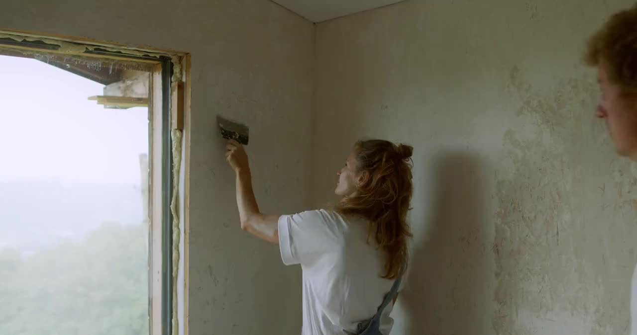 Stock footage still of two people renovating an interior wall